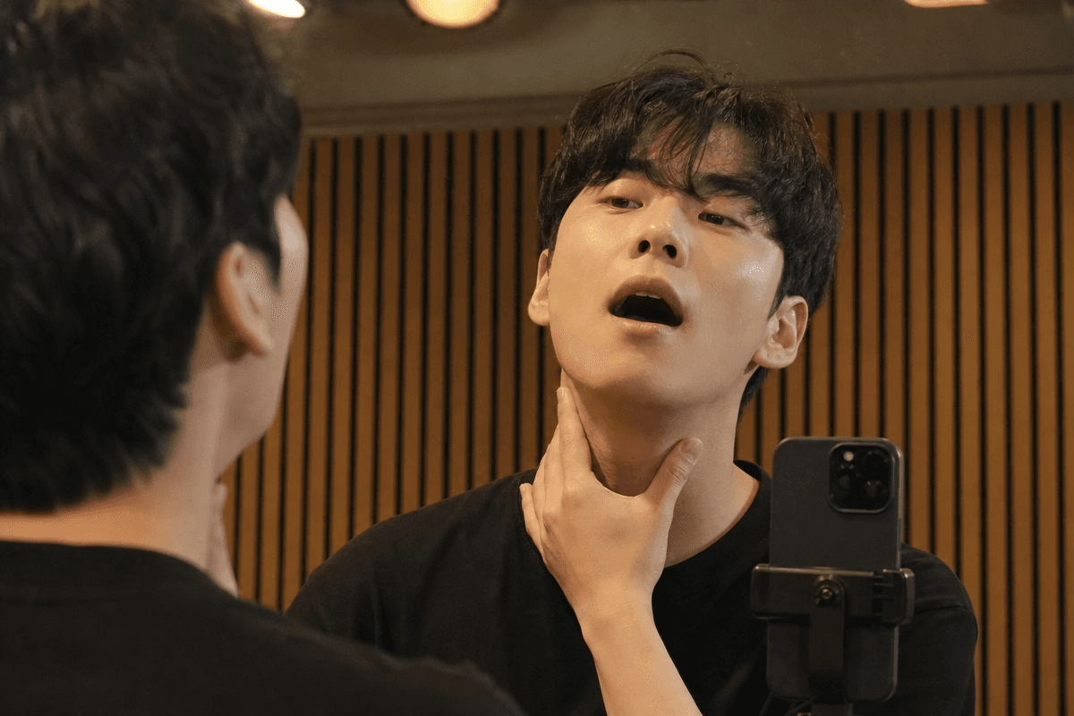 고음 연습 중 목 옆 근육을 손으로 만져 긴장을 확인하는 남성의 모습으로 고음 목 갈라짐 원인을 설명하는 장면