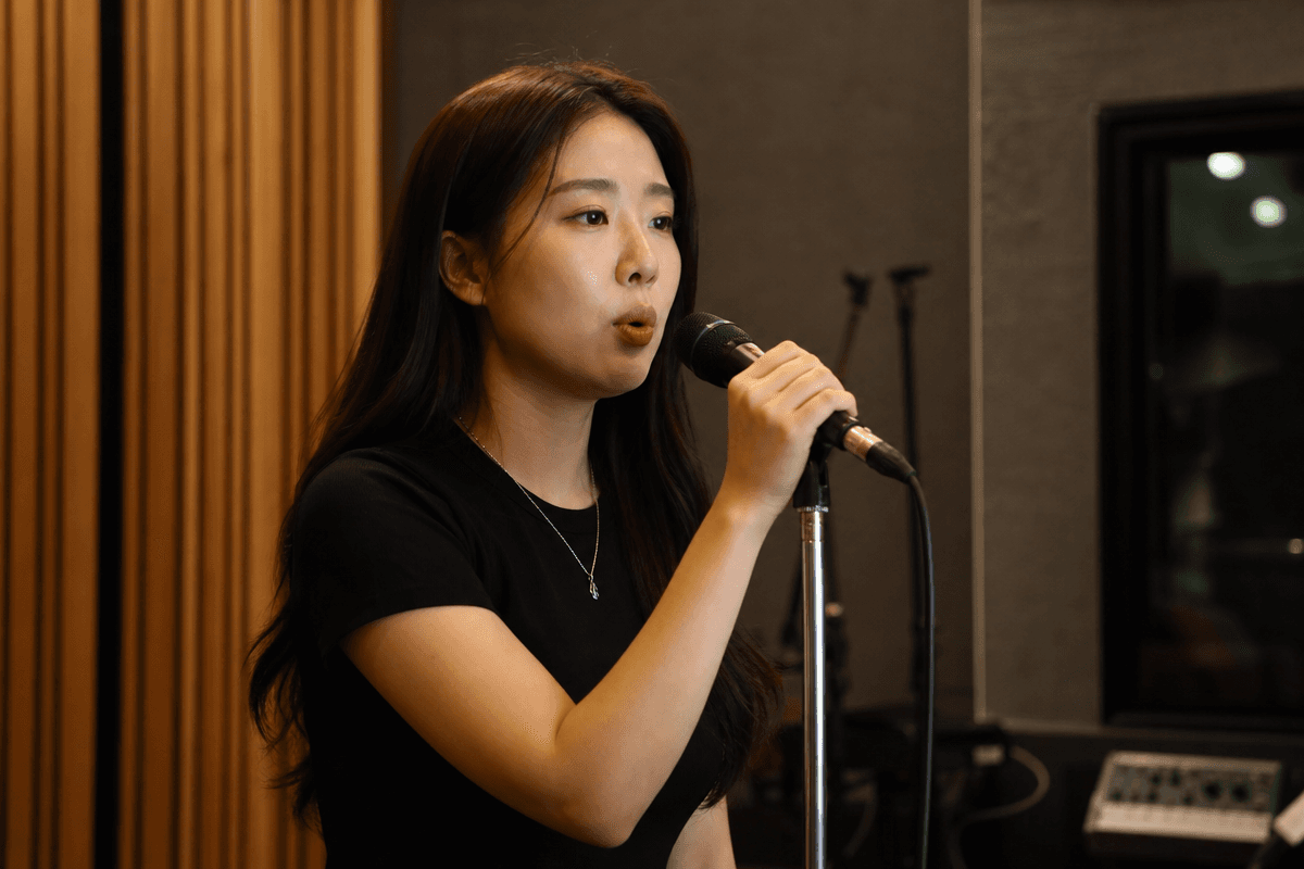 믹스보이스와 모음 조절로 고음 목 갈라짐을 완화하며 마이크로 발성 연습 중인 여성 모습
