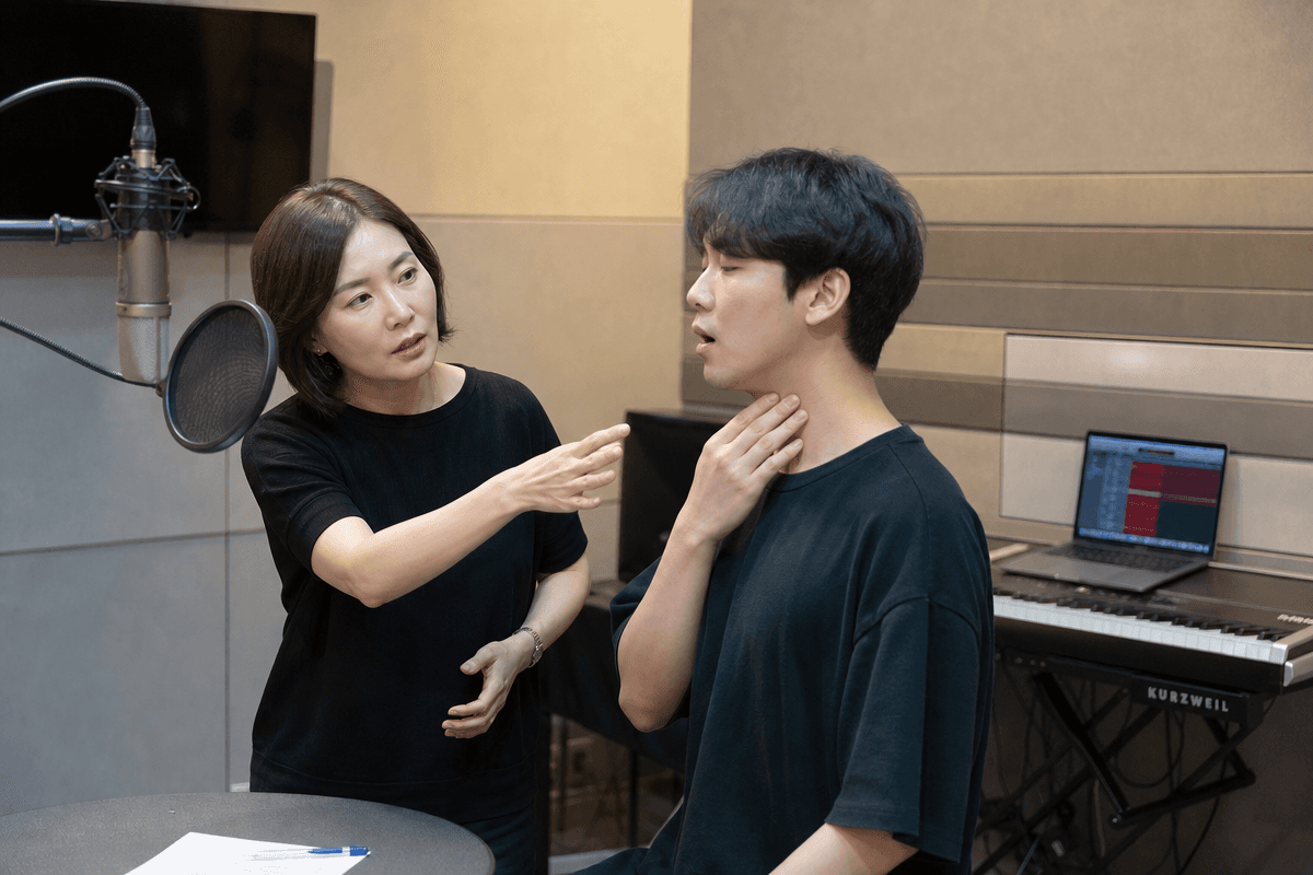 보컬 트레이너가 연습생의 진성 가성 연결 문제를 지도하며 호흡과 공명 위치를 점검하는 장면