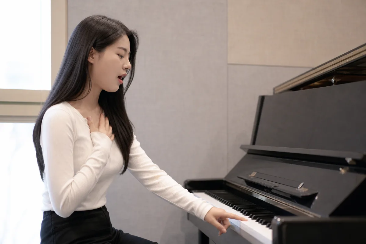 피아노 한 음을 누르며 가성 고음 전환을 연습하는 보컬 훈련 모습