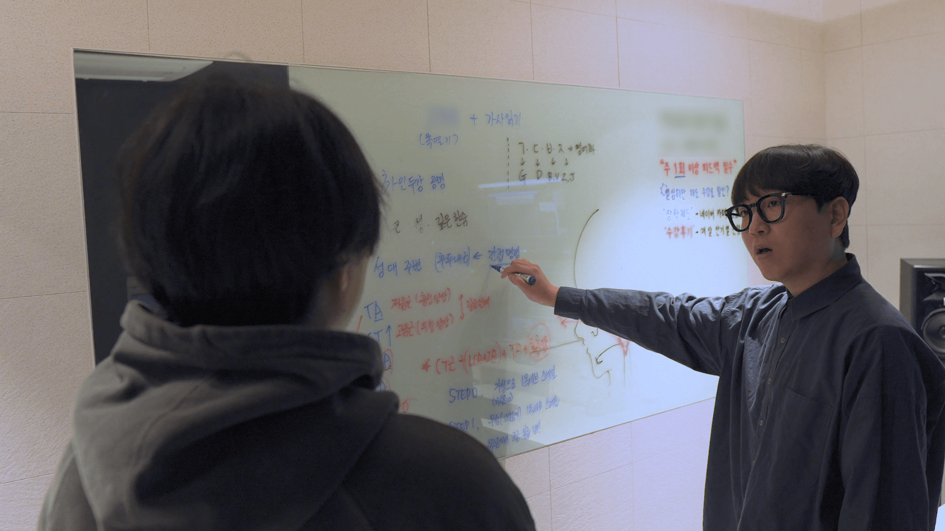 보컬 강사가 수강생에게 화이트보드 판서로 노래 이론을 가르친다.