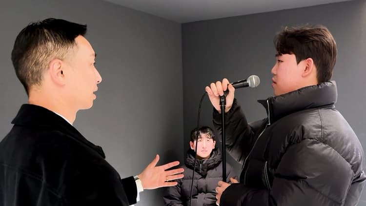 보컬 강사가 마이크 든 수강생에게 발성 지도를 한다.