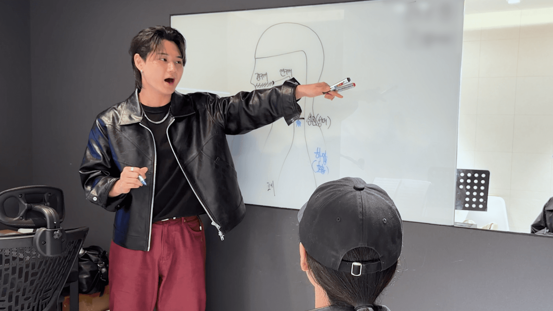 화이트보드 앞에서 발성을 설명하는 보컬 트레이너와 수강생