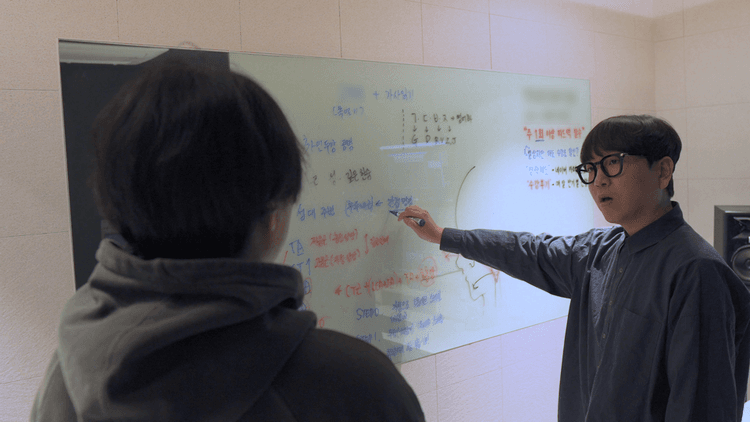 한 사람이 다른 사람을 보며 화이트보드에 적힌 내용을 마커로 가리켜 설명한다.