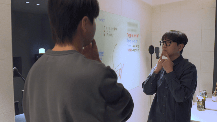 두 남자가 화이트보드 앞에서 턱에 손을 대고 발음 연습을 한다.